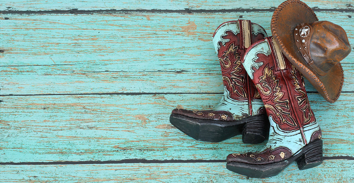 Texas cowboy boots and cowboy hat hanging on teal weathered wood