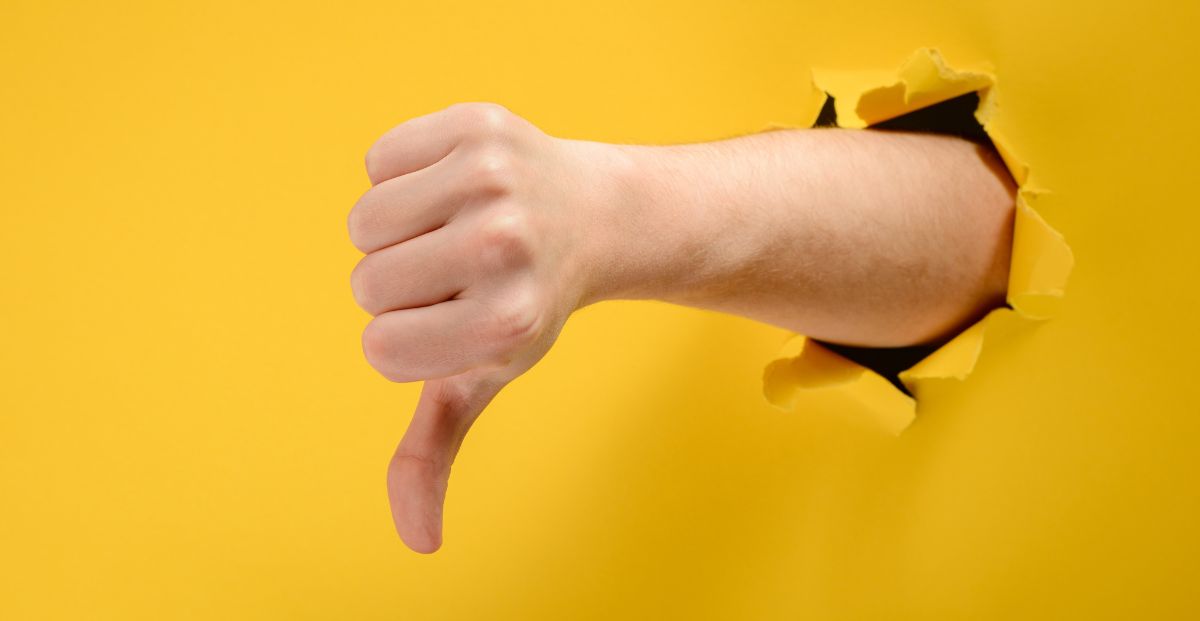 a hand with a thumbs down breaking through a yellow wall